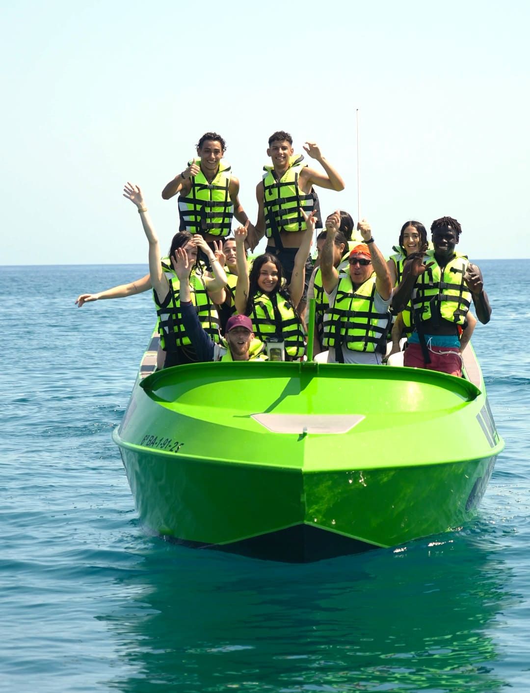 Gruppe mit Schwimmwesten winkt an Bord des grünen JetBoats