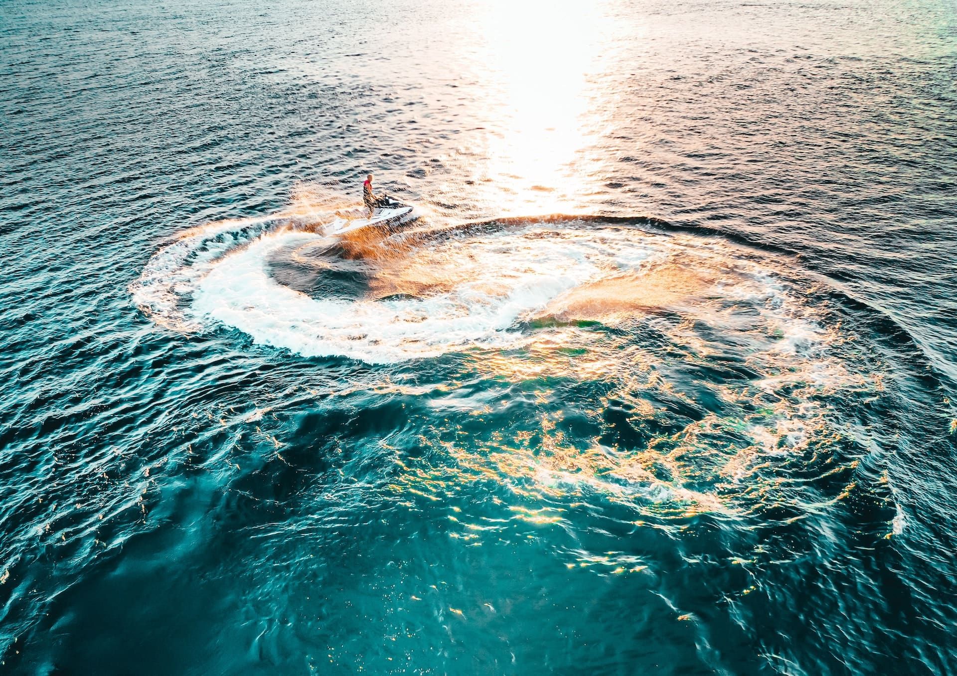 Jetski zieht bei Sonnenuntergang einen Kreis aus Gischt über das Meer